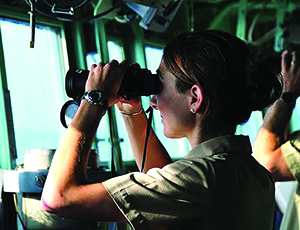 Image shows woman with binoculars overlooking the sea.