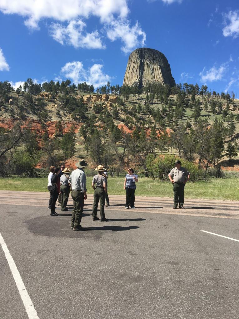 Devils Tower in the background with park rangers standing on the roadway in the foreground.