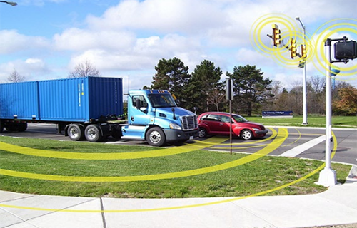 A car and a truck approach a lighted intersection. Smart technology alerts the vehicles that the light is turning yellow.