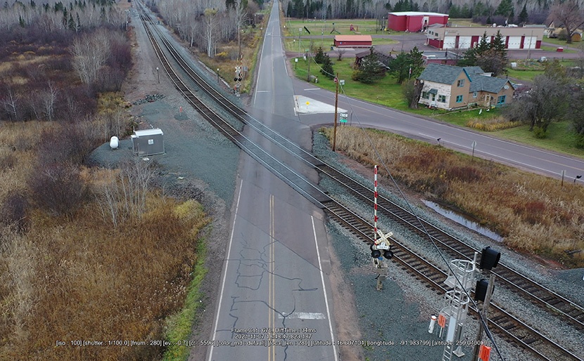An aerial view of a railroad track that curves at a crossing with a highway.