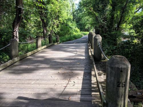 "Boardwalk with fence posts along each side. This boardwalk connects to an asphalt bicycle-pedestrian pathway."