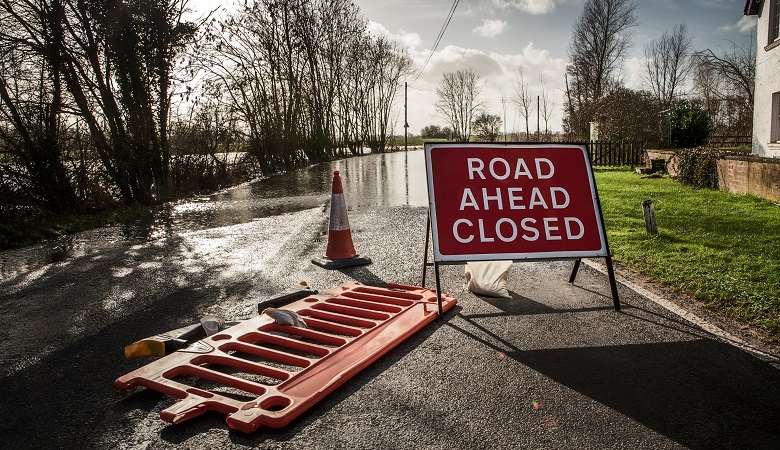 A road closed sign in front of a flooded roadway