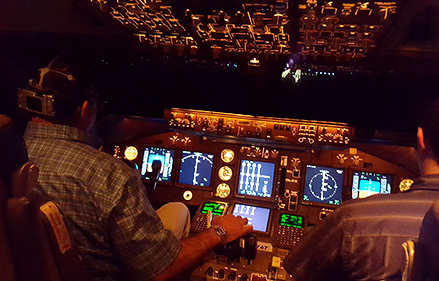 Two men sit in an aircraft cockpit, one is wearing a workload measuring device.
