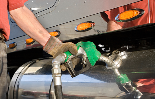 A man holds a gas nozzle while refueling a tractor trailer.