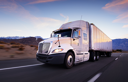A semi truck driving on a highway at sunset.