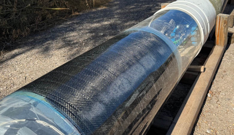 QuakeWrap’s Automated Guide Vehicle seen through a plexiglass pipe, with SuperLaminate carbon fabric in the foreground (QuakeWrap photo)