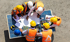 An image of six construction workers studying a plan laid out on a table outside.