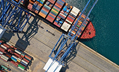 An image of a cargo ship with boxes of cargo docked at a loading dock in the ocean.