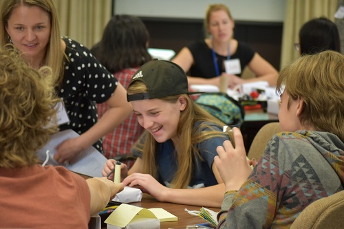 Two students, a boy and a girl, laugh while assembling cardboard blocks covered in paper.