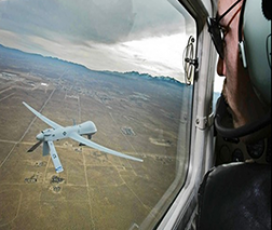 A pilot views a unmanned aircraft system outside the window of a cockpit.