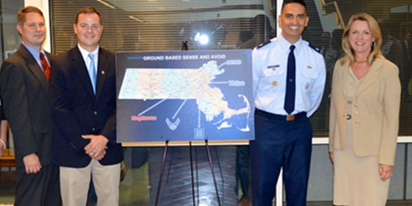 Four professional stand, smiling, beside a map of Massachusetts showing location where GBDAA technology is being implemented.