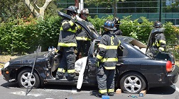 Firefighters use the Jaws of Life to cut into a car, with part of the roof now removed.