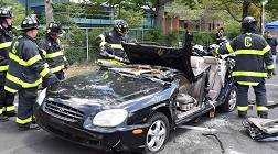 Firefighters use the Jaws of Life to cut into a car, with the roof now completely removed.
