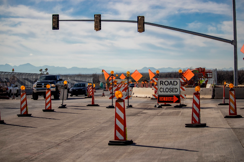 Vehicles drive near an active work zone that is cordoned off with safety cones and lights.