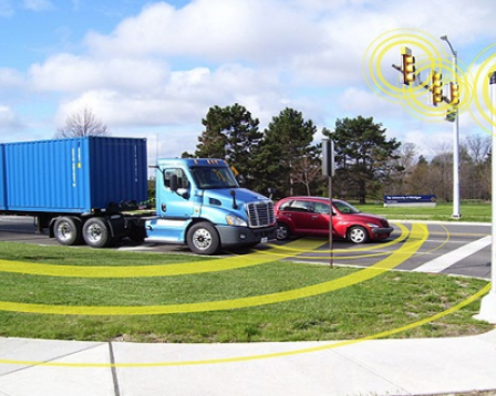 A car and a truck approach a lighted intersection. Smart technology alerts the vehicles that the light is turning yellow.