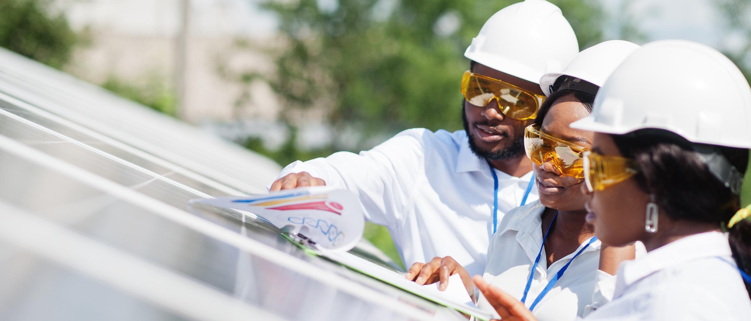 Three people with hard hats looking at plans