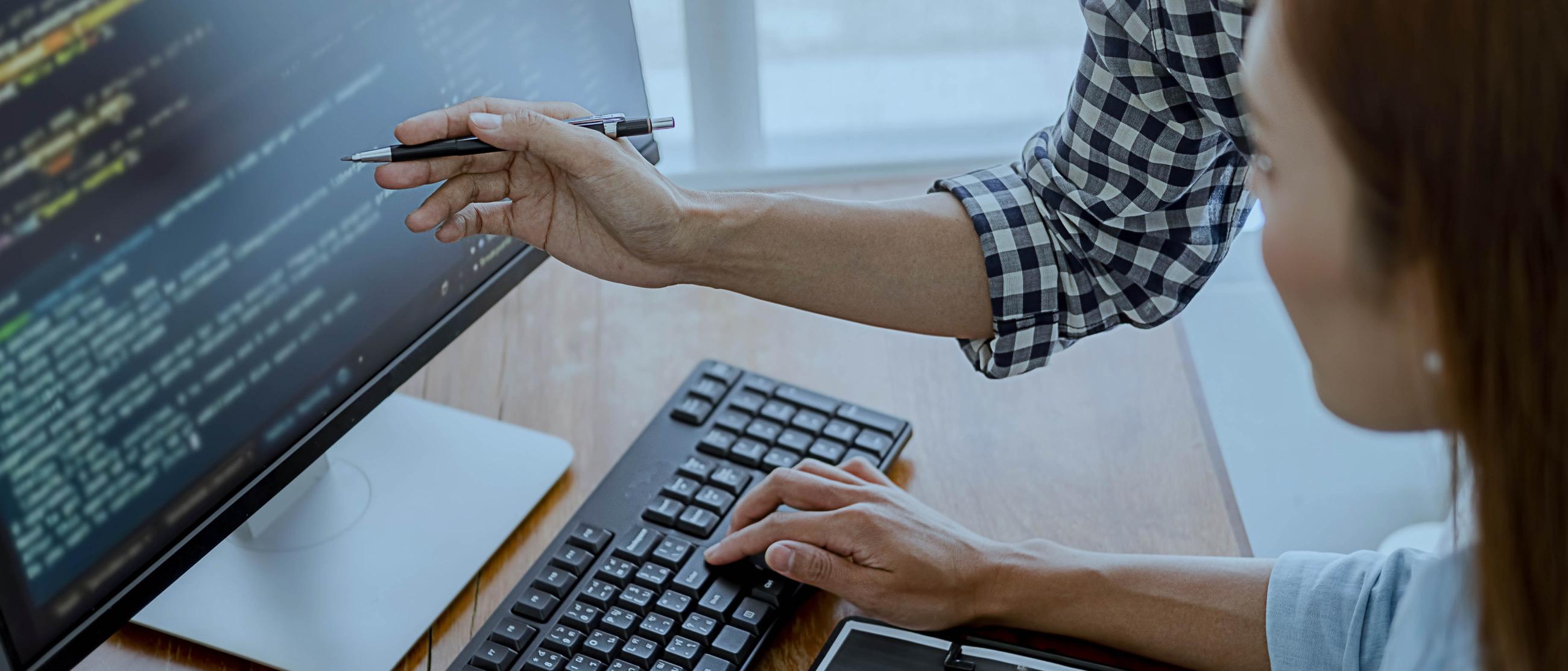 A woman standing over a desk and pointing to a computer screen
