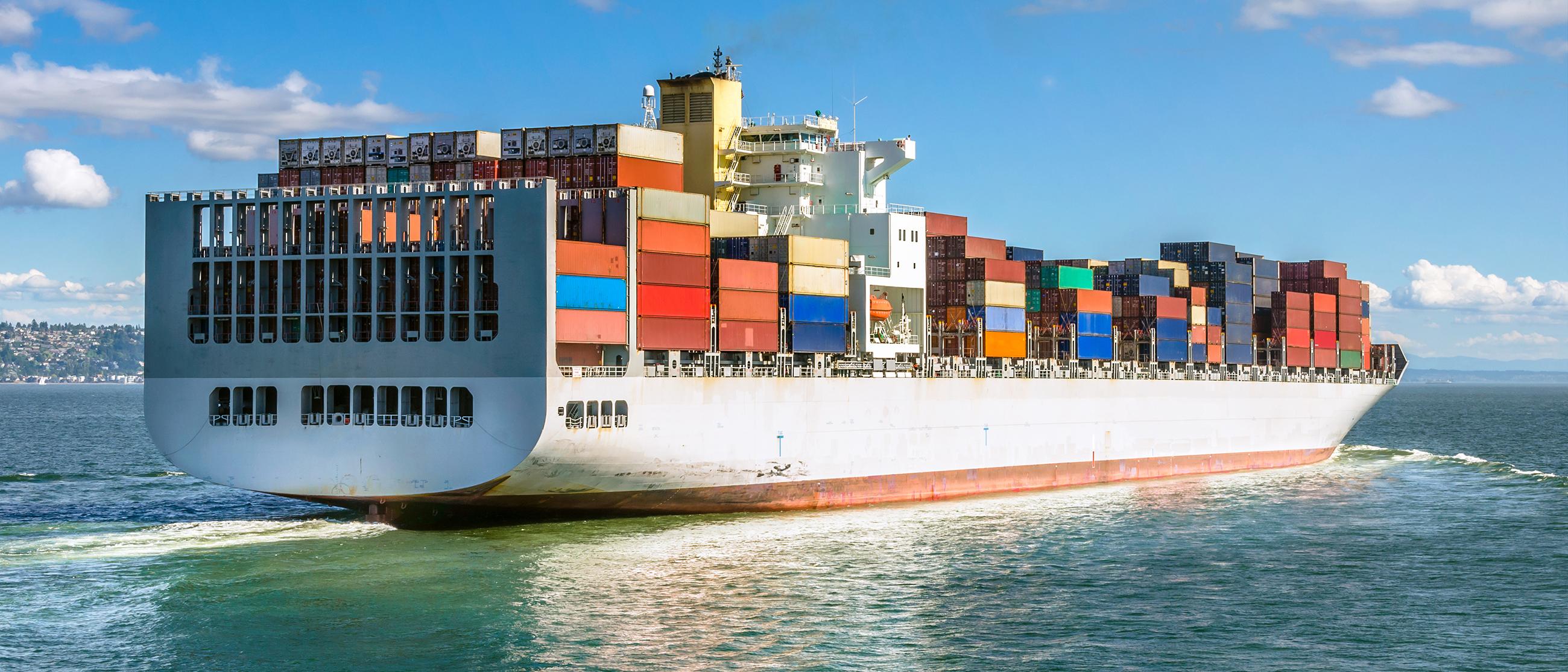 Image shows ship carrying hundreds of shipping containers on an open waterway.