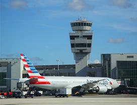 An American Airlines plain waits in front of a control tower at Miami International Airport.