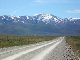 Gravel road through field with mountains in the background