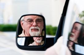 Bearded man driving vehicle and looking in car's side mirror